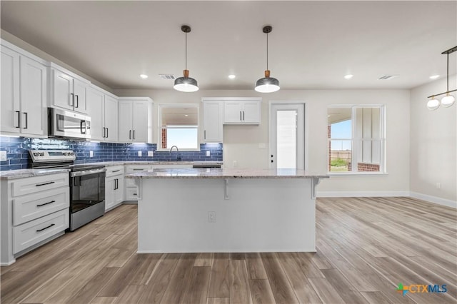 1811 Ember Dr, Temple, TX 76502 - kitchen featuring appliances with stainless steel finishes, a kitchen island, white cabinets, light wood-style flooring, and tasteful backsplash