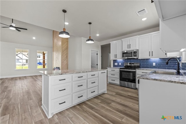 1811 Ember Dr, Temple, TX 76502 - kitchen with appliances with stainless steel finishes, a ceiling fan, a kitchen island, backsplash, and light wood finished floors