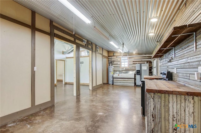 basement with stainless steel fridge with ice dispenser, a garage, and water heater