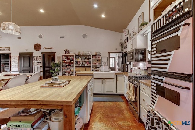 kitchen featuring lofted ceiling, a sink, white cabinetry, appliances with stainless steel finishes, and wooden counters