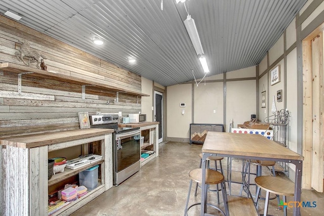 kitchen with white microwave, butcher block counters, concrete flooring, stainless steel range with electric cooktop, and open shelves