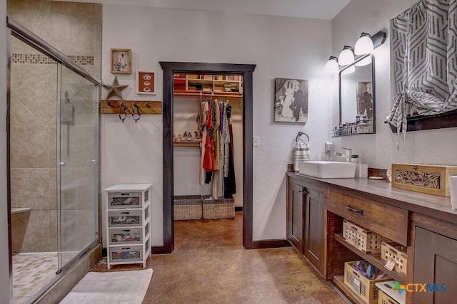 bathroom featuring a walk in closet, baseboards, a stall shower, a textured wall, and vanity