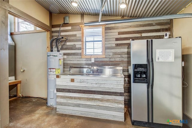 kitchen with wood walls, concrete flooring, stainless steel fridge with ice dispenser, electric water heater, and vaulted ceiling