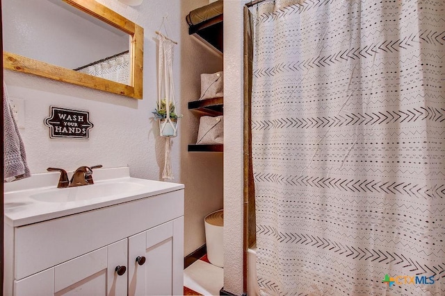 full bathroom with a shower with curtain, a textured wall, and vanity