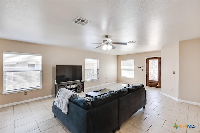 living area with light tile patterned floors, a ceiling fan, visible vents, and baseboards