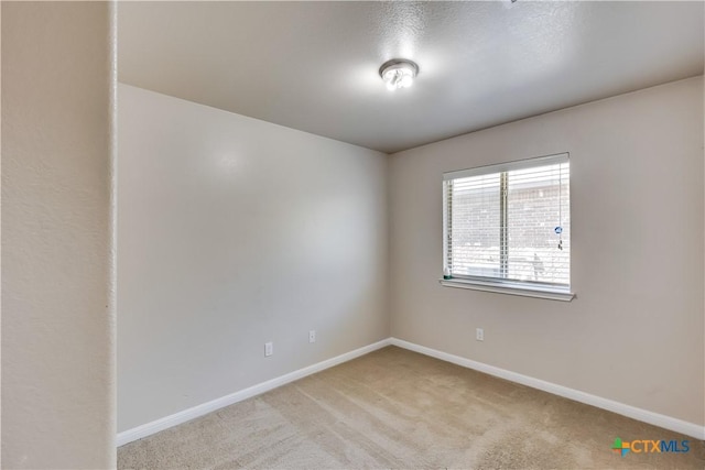 empty room featuring baseboards and light carpet