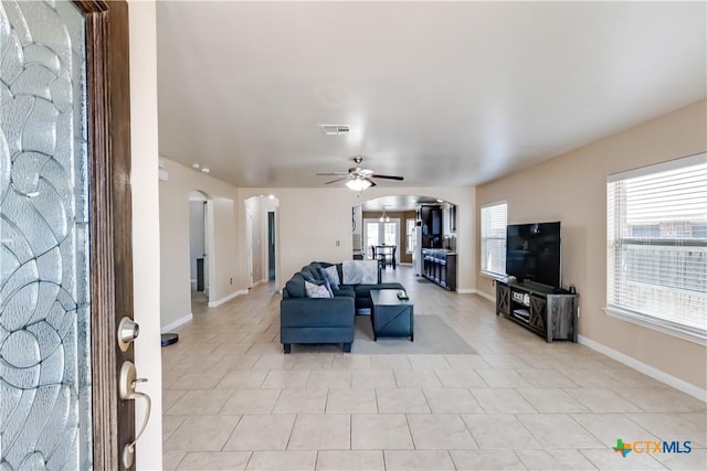 living room featuring visible vents, a ceiling fan, arched walkways, and baseboards