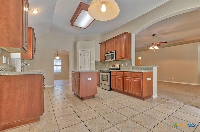 kitchen with ceiling fan, backsplash, a kitchen island, light tile patterned flooring, and appliances with stainless steel finishes