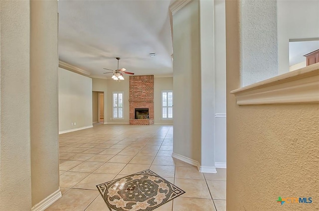 unfurnished living room with a brick fireplace, light tile patterned floors, crown molding, and ceiling fan