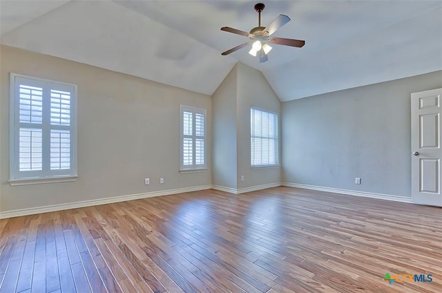 empty room with ceiling fan, light hardwood / wood-style floors, a wealth of natural light, and vaulted ceiling