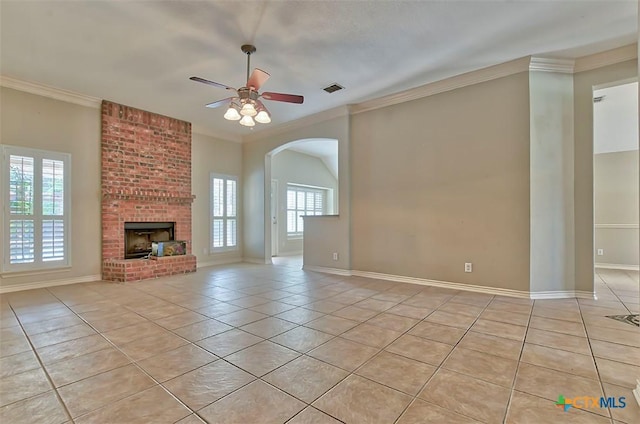 unfurnished living room featuring ceiling fan, a fireplace, light tile patterned flooring, crown molding, and a healthy amount of sunlight