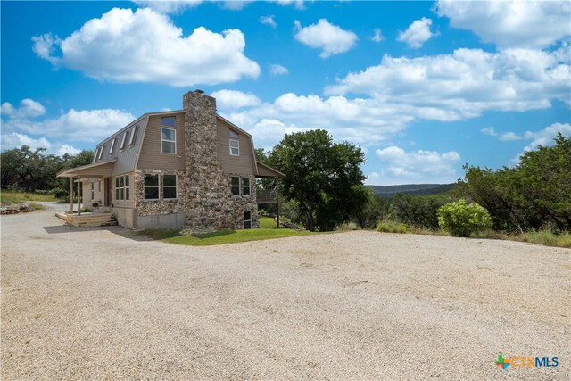 514 Eden Ranch Dr, Canyon Lake, TX 78133 - view of side of property featuring a gambrel roof, gravel driveway, stone siding, and a chimney
