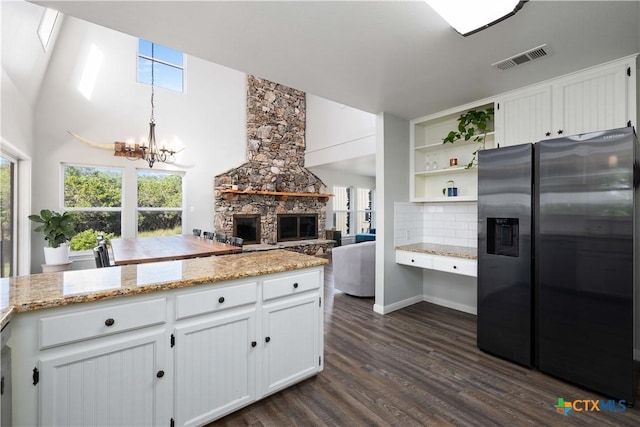 514 Eden Ranch Dr, Canyon Lake, TX 78133 - kitchen featuring stainless steel fridge, a stone fireplace, a chandelier, dark wood-type flooring, and white cabinetry