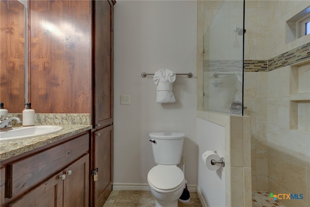 bathroom with toilet, vanity, tile patterned flooring, and a tile shower