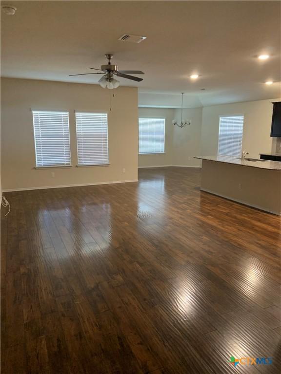 empty room with recessed lighting, baseboards, ceiling fan with notable chandelier, and dark wood-style floors