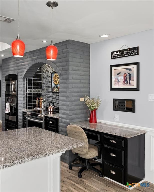 kitchen with pendant lighting, stainless steel appliances, light stone countertops, and hardwood / wood-style flooring