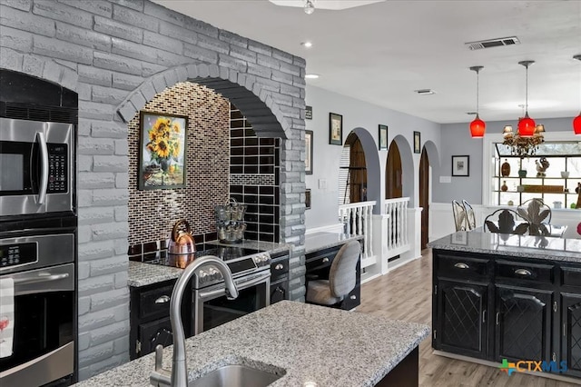 kitchen with appliances with stainless steel finishes, decorative light fixtures, sink, decorative backsplash, and light hardwood / wood-style floors