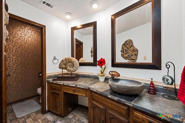 bathroom with vanity, toilet, and a textured ceiling