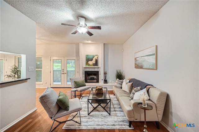 living room with french doors, a fireplace, a textured ceiling, hardwood / wood-style flooring, and ceiling fan