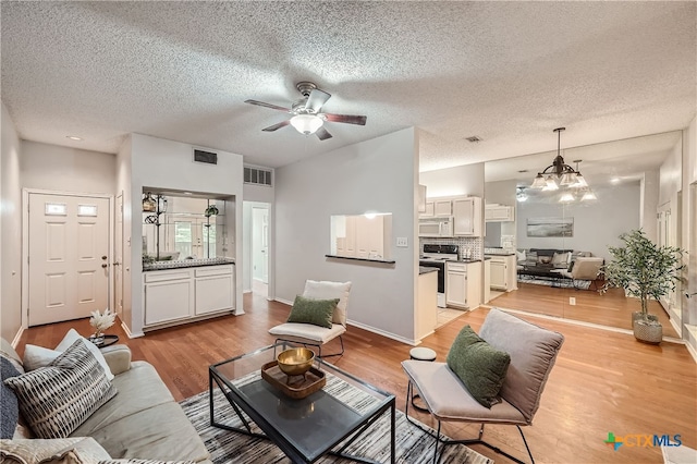 living room featuring ceiling fan with notable chandelier, light hardwood / wood-style floors, and a textured ceiling