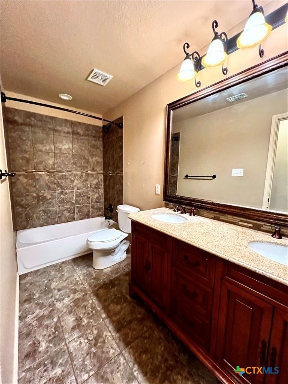 full bathroom with vanity, toilet, a textured ceiling, and tiled shower / bath combo