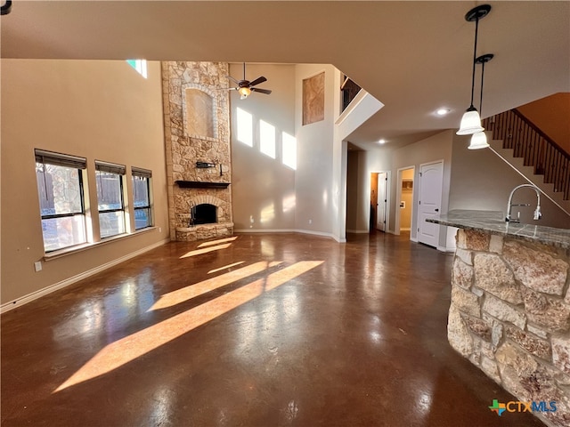 unfurnished living room with a fireplace, a towering ceiling, ceiling fan, and sink