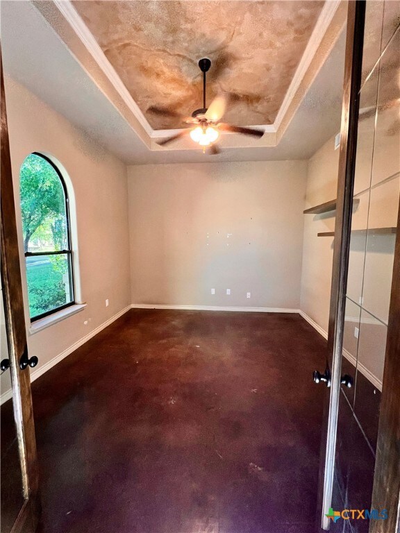 empty room with a tray ceiling, dark carpet, ceiling fan, and crown molding