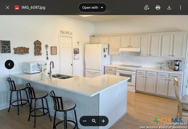 1254 Village Shore Dr, Canyon Lake, TX 78133 - kitchen featuring white appliances, under cabinet range hood, a sink, decorative backsplash, and a kitchen bar