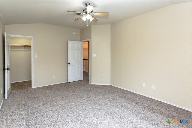 unfurnished bedroom featuring lofted ceiling, a walk in closet, carpet flooring, and baseboards