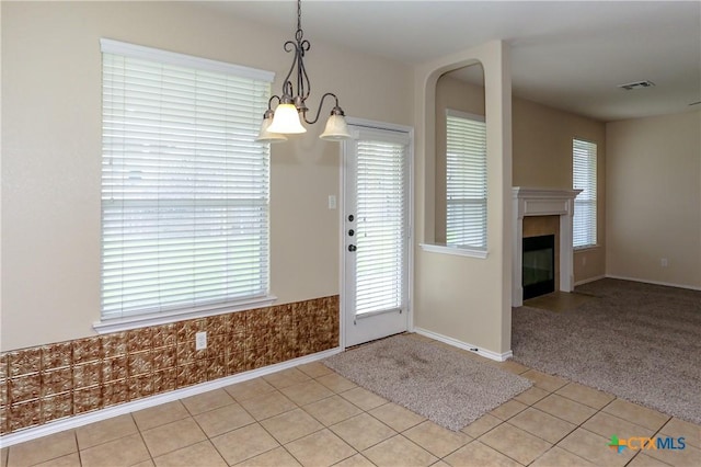 unfurnished dining area featuring light carpet, visible vents, a tiled fireplace, and light tile patterned floors