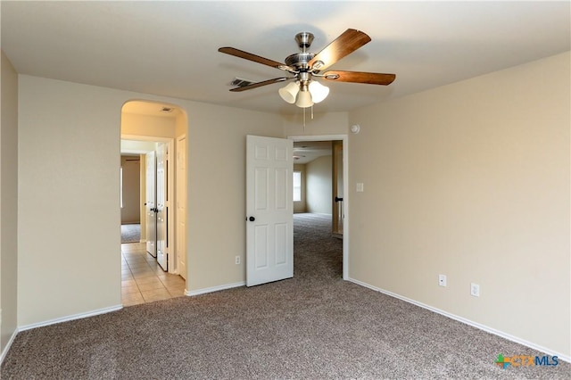 unfurnished bedroom featuring light tile patterned floors, baseboards, arched walkways, a ceiling fan, and light colored carpet