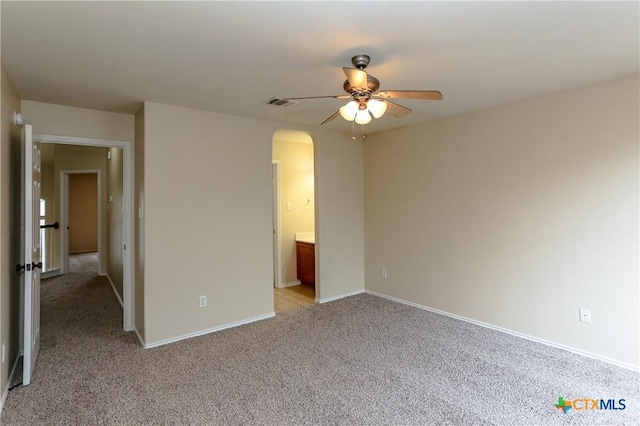 unfurnished bedroom featuring arched walkways, light colored carpet, visible vents, connected bathroom, and baseboards