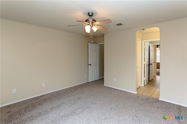 spare room with ceiling fan, arched walkways, light carpet, visible vents, and baseboards