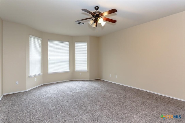 carpeted empty room with baseboards, visible vents, and a ceiling fan