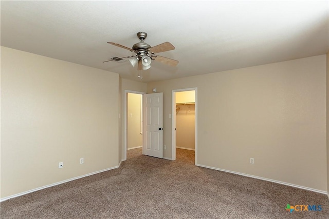 unfurnished bedroom featuring carpet, baseboards, a walk in closet, and a ceiling fan