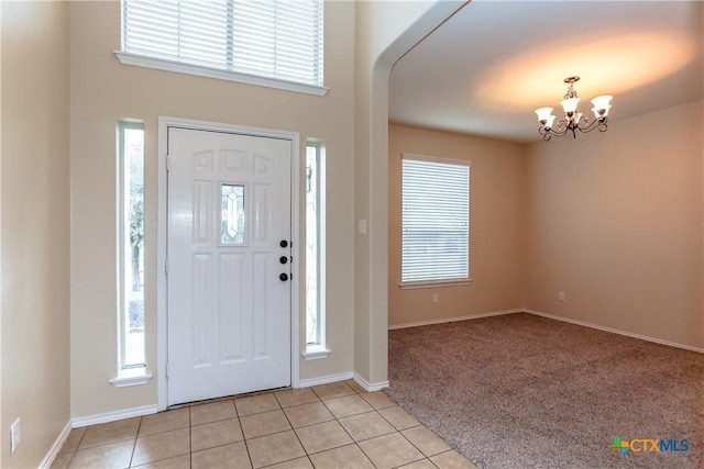 foyer featuring light colored carpet, a healthy amount of sunlight, a notable chandelier, and light tile patterned floors