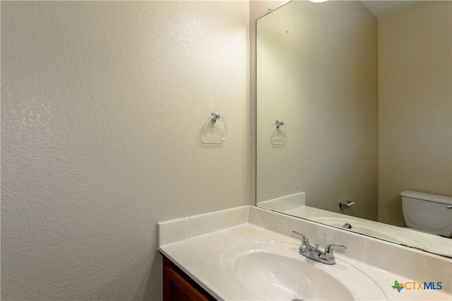 bathroom with toilet, a textured wall, and vanity