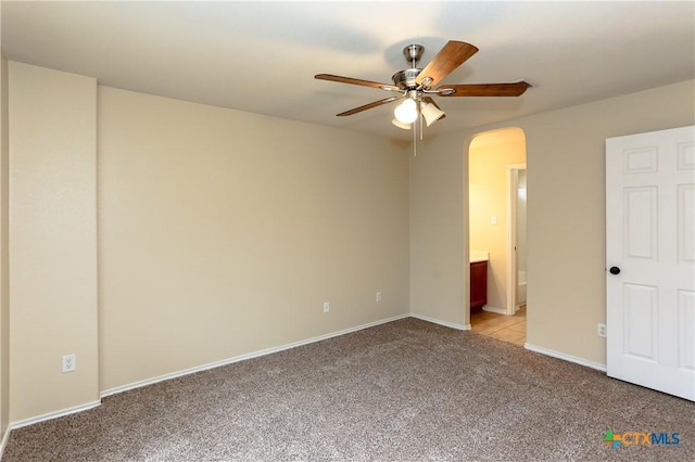 unfurnished bedroom featuring arched walkways, ensuite bathroom, light carpet, ceiling fan, and baseboards