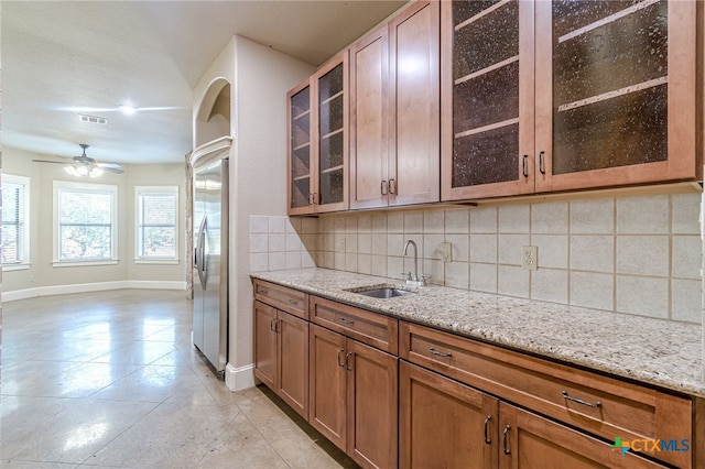 kitchen with backsplash, sink, ceiling fan, light stone countertops, and stainless steel refrigerator