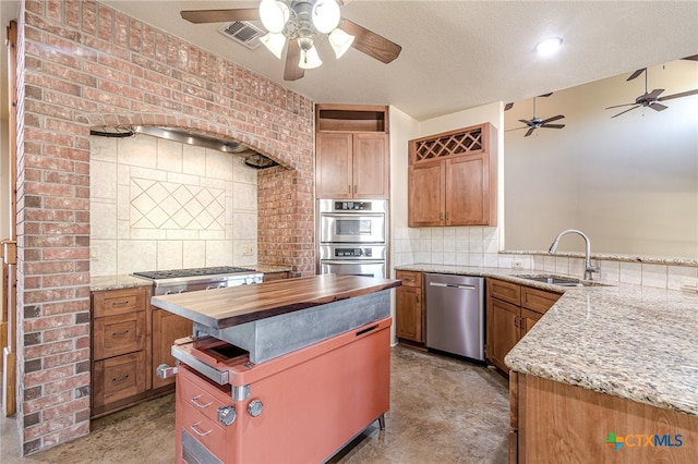 kitchen with sink, wood counters, backsplash, a textured ceiling, and appliances with stainless steel finishes