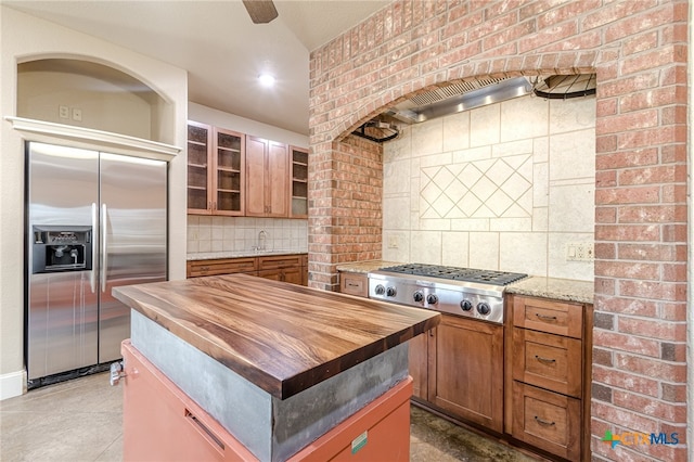 kitchen with butcher block counters, sink, backsplash, a kitchen island, and appliances with stainless steel finishes