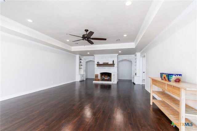 living room with dark wood-type flooring, ornamental molding, ceiling fan, a tray ceiling, and a fireplace