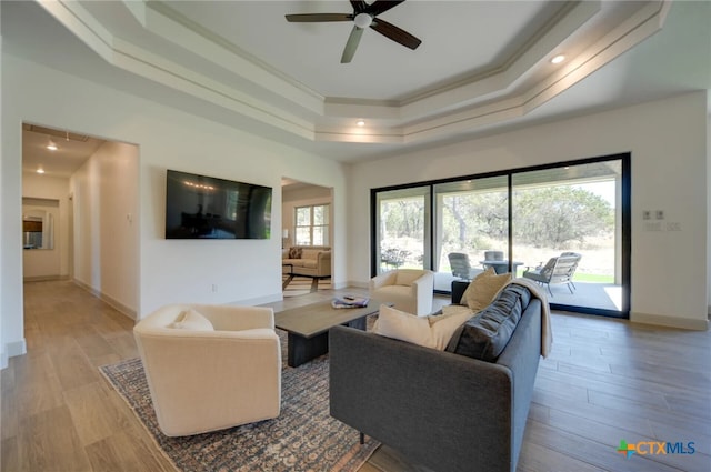 living room featuring ceiling fan, light wood-type flooring, crown molding, and a tray ceiling