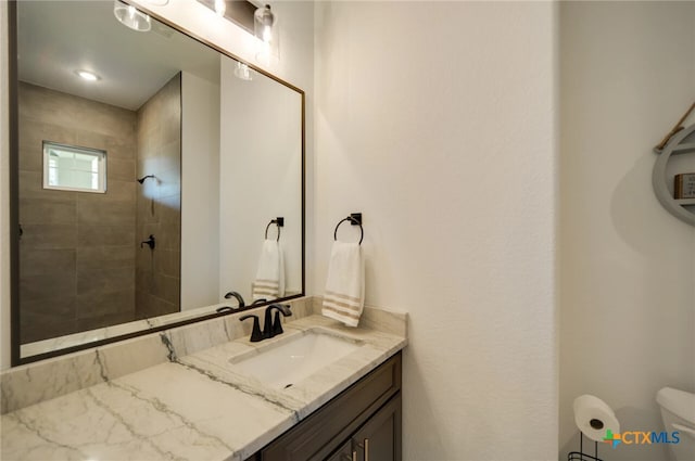 bathroom with toilet, vanity, and a tile shower