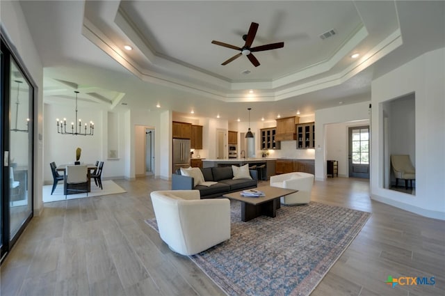 living room with light hardwood / wood-style floors, ceiling fan with notable chandelier, crown molding, and a tray ceiling