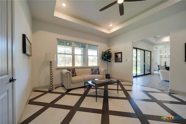 living room with ceiling fan with notable chandelier, ornamental molding, and a raised ceiling