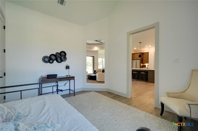 bedroom featuring stainless steel fridge, light wood-type flooring, and lofted ceiling