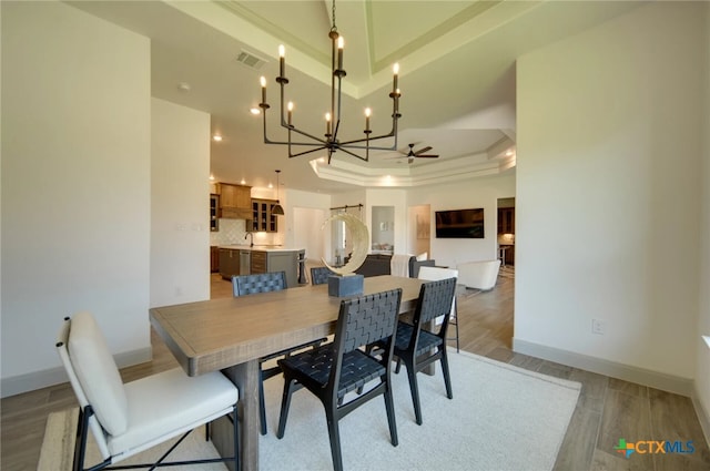 dining room featuring ceiling fan, sink, light wood-type flooring, and a tray ceiling