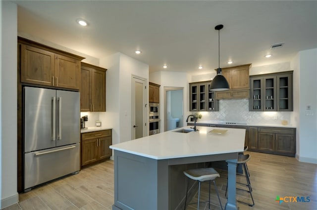 kitchen with stainless steel appliances, light hardwood / wood-style floors, a center island with sink, sink, and decorative light fixtures