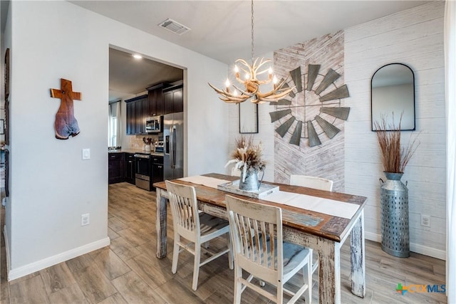 dining area with light wood finished floors, visible vents, baseboards, and an inviting chandelier